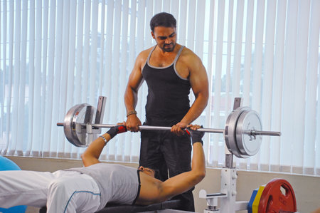 Personal trainer assisting a man lifting a barbell in a fitness centerのeditorial素材