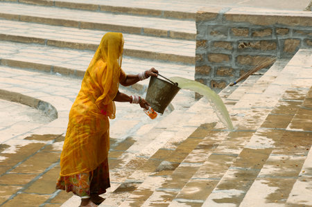 Indian woman pouring water from a bucket on the steps of a templeのeditorial素材