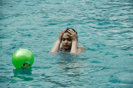 Young man swimming in the pool with a green inflatable ball.のeditorial素材