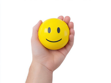 A hand gently holds a yellow, round smiley face ball. The image conveys a sense of positivity and stress relief. The bright color and simple design create a cheerful and inviting visual.の素材