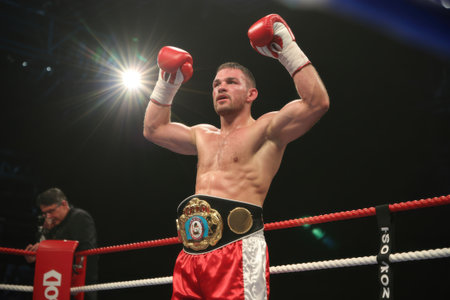 A triumphant boxer raises his gloved fists in celebration, adorned with a championship belt, basking in the glory of his hard-fought victory in the boxing ring.の素材
