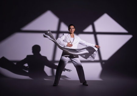 A performer dramatically spins a large, elaborate metallic whisk. Dramatic geometric lighting and shadows create an artistic and theatrical atmosphere on a dark stage.の素材