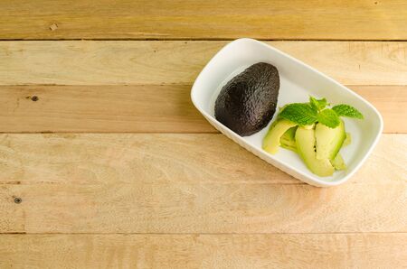 Plate with Avocado and sliced avocado with mint on top on wooden backgroundの写真素材