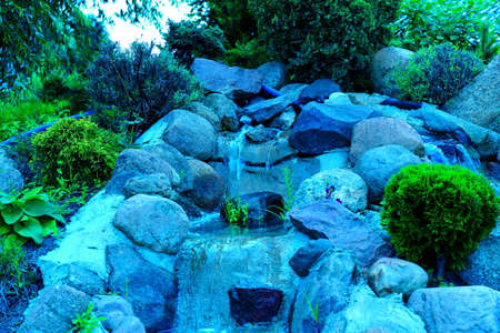 A small water cascade built of natural stones and rocks in the backyard garden