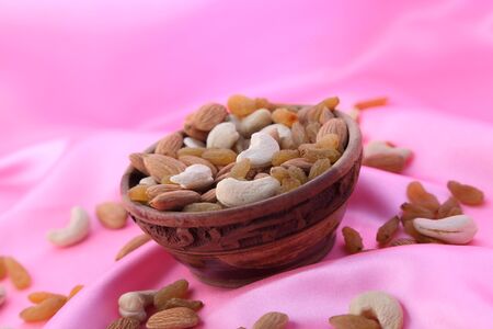 Delicious and healthy mixed dried fruit, nuts and seeds in a wooden bowl on pink silky background.の写真素材