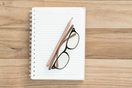 Overhead of open notebook with glasses and pencil on a wooden backgroundの写真素材