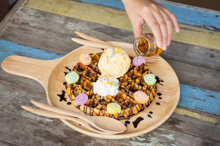 pouring caramel on vanilla ice cream with waffle on wooden dishの写真素材
