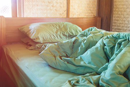 green pillow and blanket with wrinkle messy on bed in vintage wooden bedroom with lighting upper left side, from sleeping in a long night winter.の写真素材