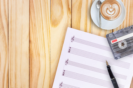 Sheet music, fountain pen, tape cassette and coffee latte on wooden tableの写真素材
