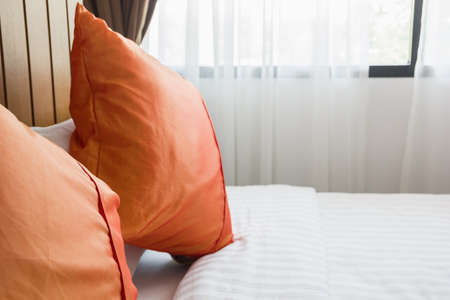 orange pillow and white blanket on bed in bedroom with lighting upper right sideの写真素材