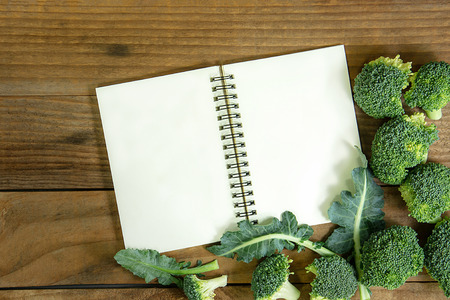 blank notebook with fresh broccoli on wooden tableの写真素材