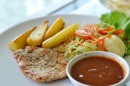 Grilled pork steak served with chips, potatoes and vegetables , tomato sauceの写真素材