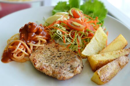 Grilled pork steak served with chips, potatoes and vegetables , spaghetti  の写真素材