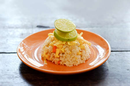  fried rice served with omelet  slice and lemon slice , on wood table