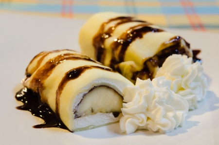 banana crepe rolls filled  with white cream and banana,   topping with chocolate  syrup served with whipping creamの写真素材