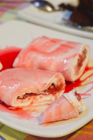  crepe rolls filled  with white cream and strawberry,   topping with strawberry  syrup  served with whipping cream on dishの写真素材