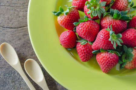 still life of fresh red strawberries on dish with spoon over wooden backgroundの写真素材