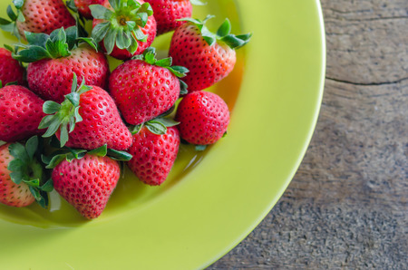 still life of fresh red strawberries on green dish over wooden backgroundの写真素材