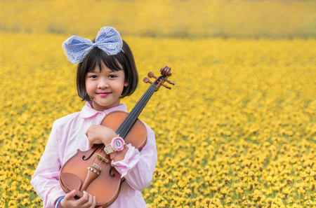 asian cute little girl with violin in  yellow flower fieldの写真素材