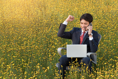 asian businessman  talking on smartphone and looking at laptop outdoorの写真素材