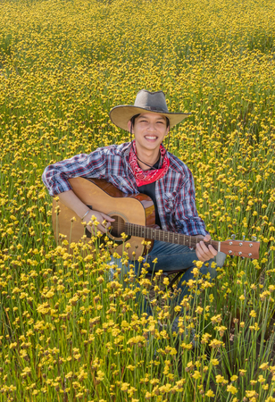 Asian farmer sitting in his bright yellow field with guitar