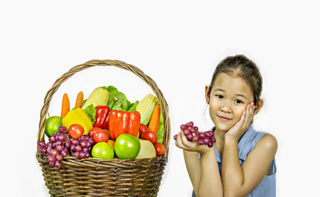 Smiling asian little girl  with fruits and vegetables in basket over white backgroundの写真素材