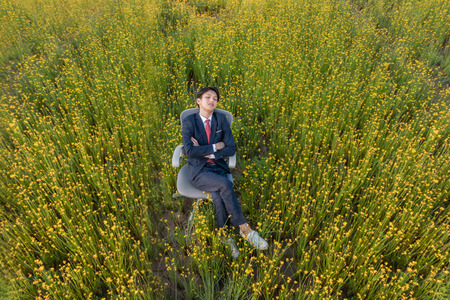 Asian businessman is lying on a chair in a large yellow flower fieldの写真素材