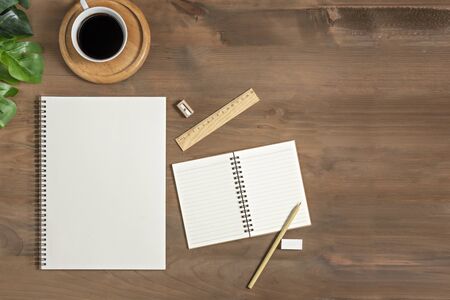 Flat lay of wooden office desk table with blank notebook, supplies and coffee cup. Top view with...