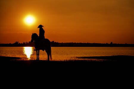 silhouette cowboy on horseback during nice sunset landscape backgroundの写真素材