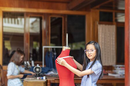 asian little girl dressmaker measuring the  dummy and looking at camera with smile while standing in workshopの写真素材