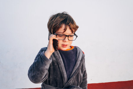 Child with a smartphone drinking coffee at breakfast while using his mobile phone to call, chat and read the newsの写真素材