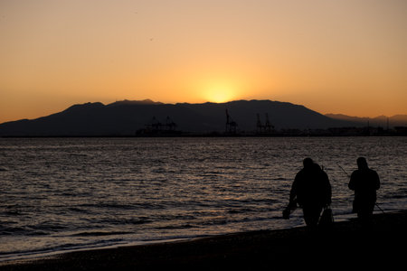 Silhouette of two fishermen returning home after finishing fishing during sunsetの写真素材