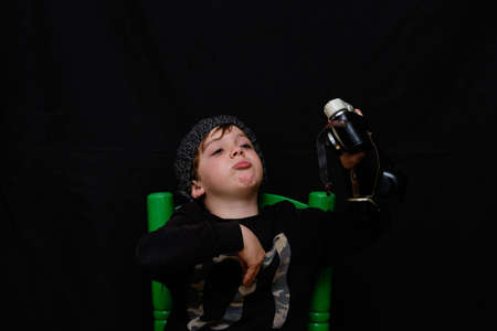 Five-year-old boy in a wool cap taking photos and selfies with an old analog camera on a black backgroundの写真素材