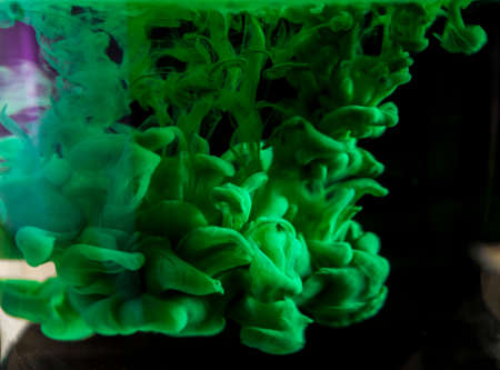 Green acrylic paint creates abstract shapes in water