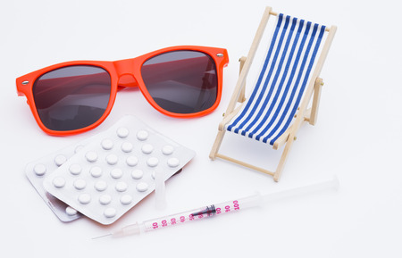 Image shows a deckchair sunglasses pills and a injectionの写真素材