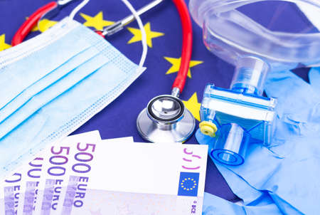 The photo shows a mouth and nose protector with disposable gloves, Cash and a stethoscope on a European flagの写真素材