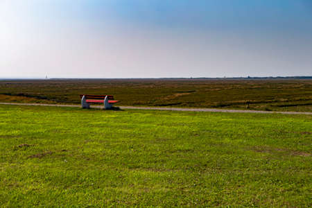The photo shows a park bench, overlooking a marshy meadow in the sunshineの写真素材