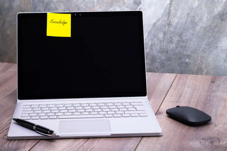 The photo shows a notebook on a wooden table, on the display is stuck the message knowledge