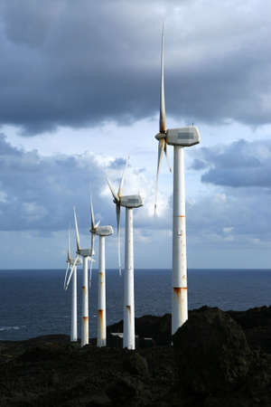 A row of wind wheels at the coast of a volcanic island generating clean power in front of a stormy skyの写真素材