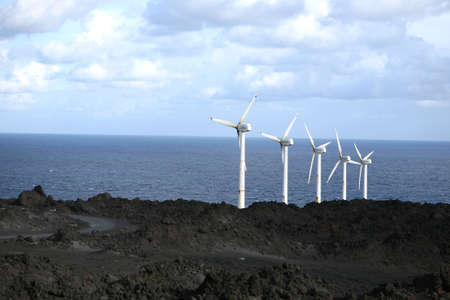 A row of wind wheels at the coast of a volcanic island generating clean powerの写真素材