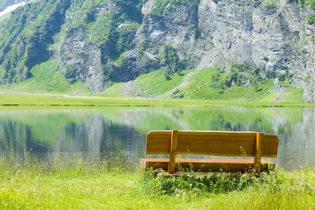 wooden bench in front of a beautiful mountain lakeの写真素材