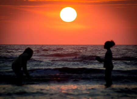 Children Playing at the Beach at Sunset Timeの写真素材
