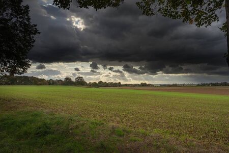 A wide view over a harvested field under a dramatic sky.の写真素材