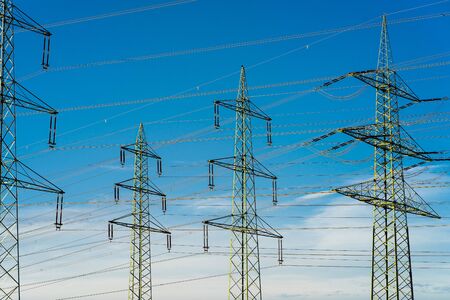 High-voltage pylons against a blue, cloudy sky.の写真素材