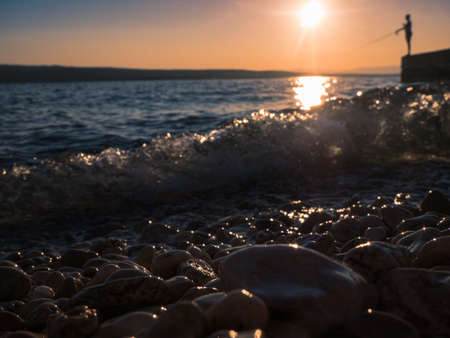 Mysterious view of stones and pebbles in water after sunset in summer. A silhouette of an angler in the background.の写真素材