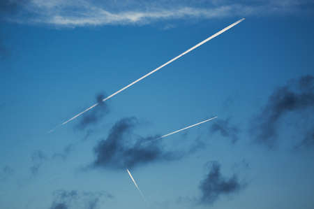 The contrails of several airplanes pervade the blue sky with clouds.