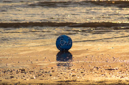 A ball lost on the beach in the orange light of the setting sun.の写真素材