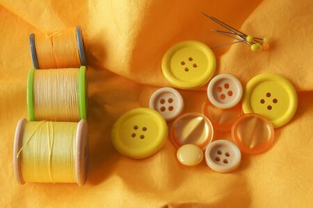 A collection of haberdashery items with a yellow theme - buttons, dressmaker's pins and cotton on bobbins. All on a piece of yellow fabric.の写真素材
