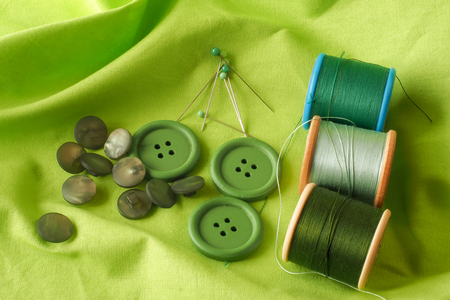A collection of haberdashery items with a green theme - buttons, dressmaker's pins and cotton on bobbins. All on a piece of green fabric.の写真素材