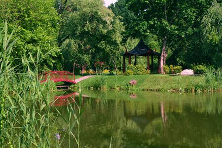 A red bridge leading to a traditional pogda near a lakeの写真素材
